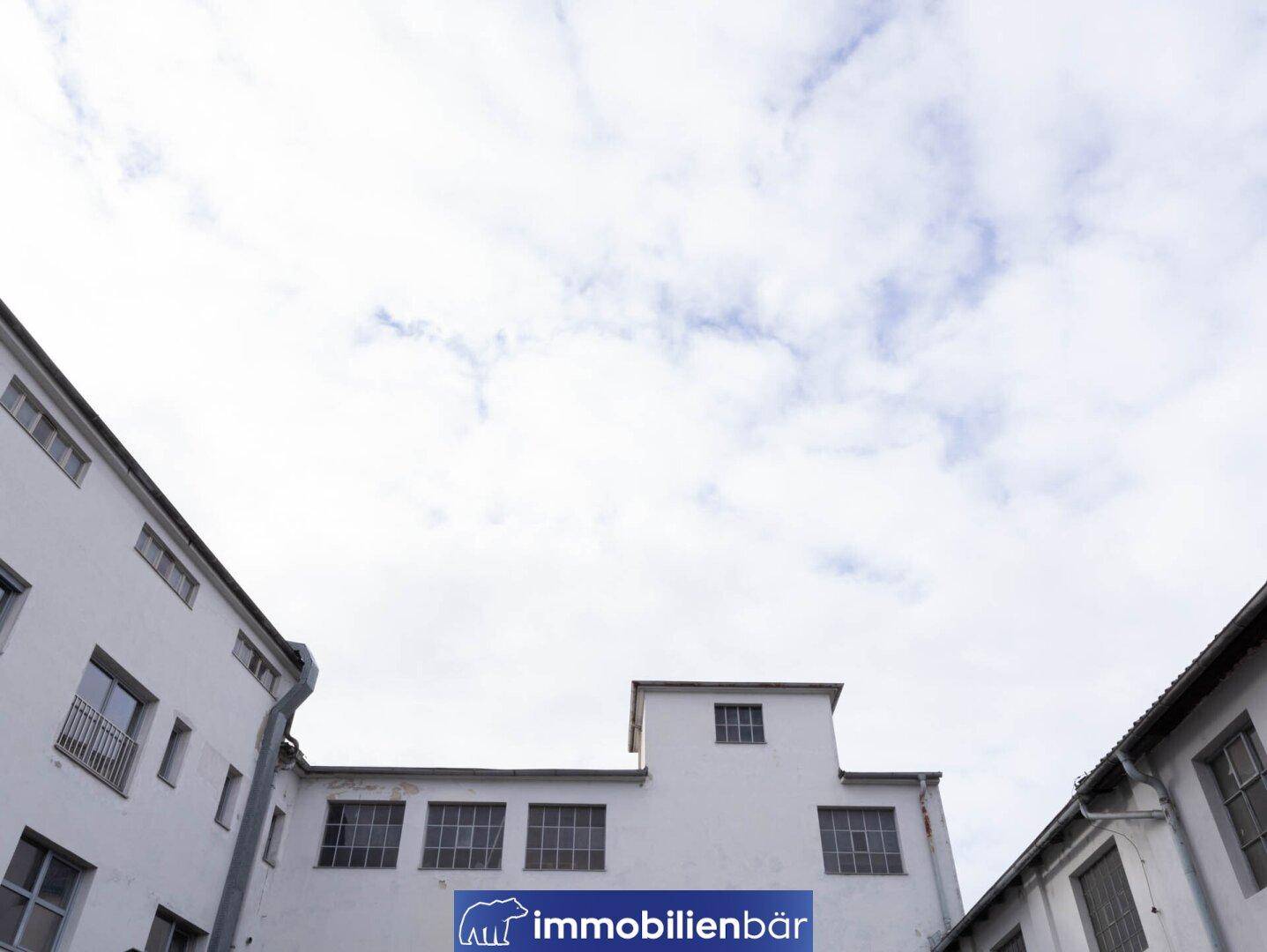 Oberer Teil des Gebäudes mit Fenstern und Dachlinie, aufgenommen unter einem bewölkten Himmel.