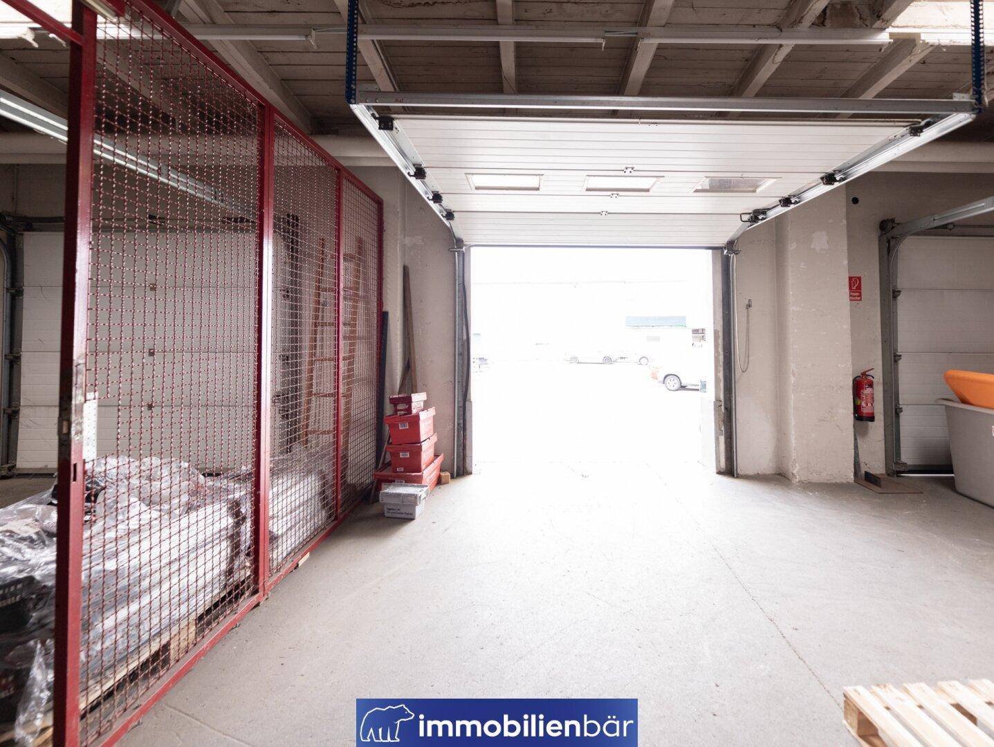 Innenansicht einer Laderampe mit offenem Tor, Betonboden und einem Metallgitterbereich.