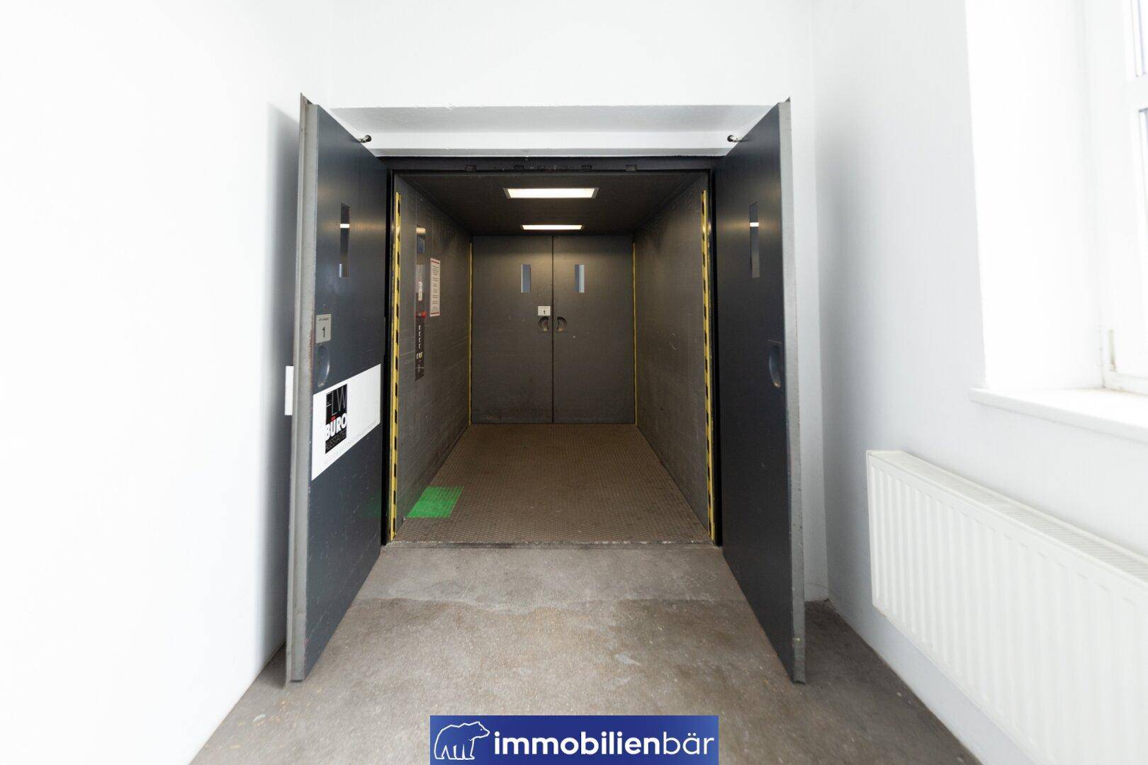 Offener Aufzug mit dunklen Türen und einem Teppichboden im Inneren, bereit zur Nutzung.