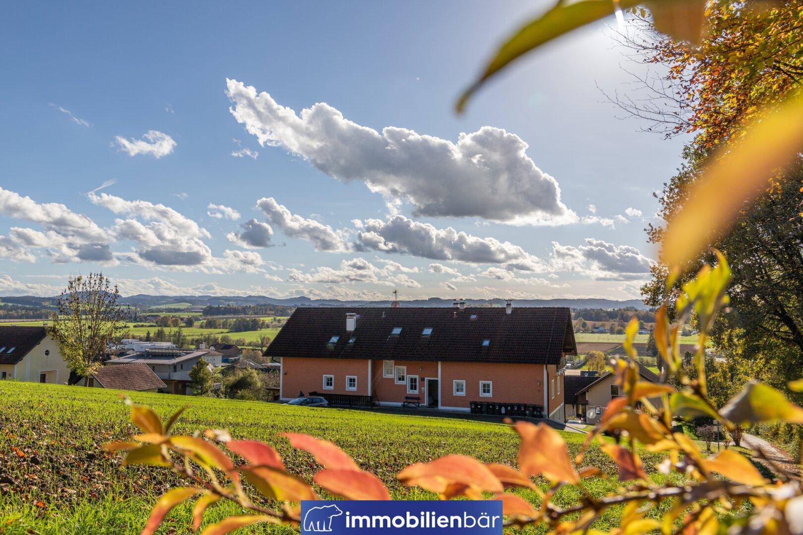 Wohnhaus in ländlicher Umgebung mit weitem Blick über grüne Hügel unter blauem Himmel und Wolken.