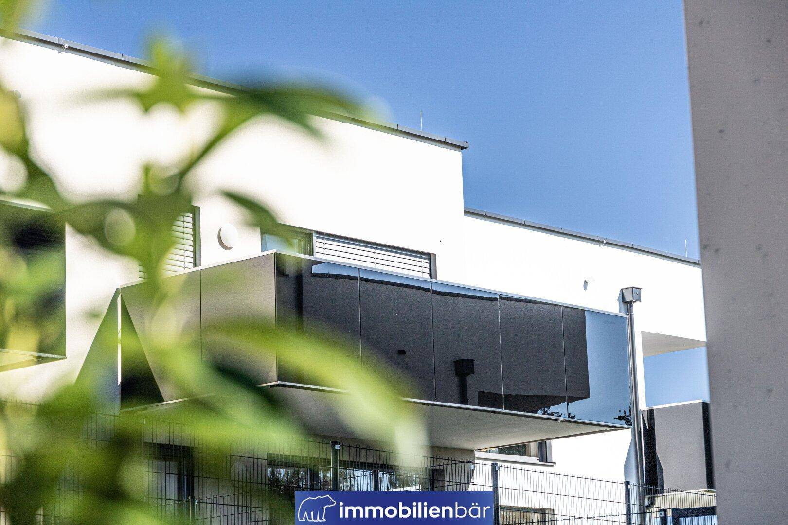 Moderner Balkon mit dunkler Glasbrüstung an der Fassade eines Neubaus.