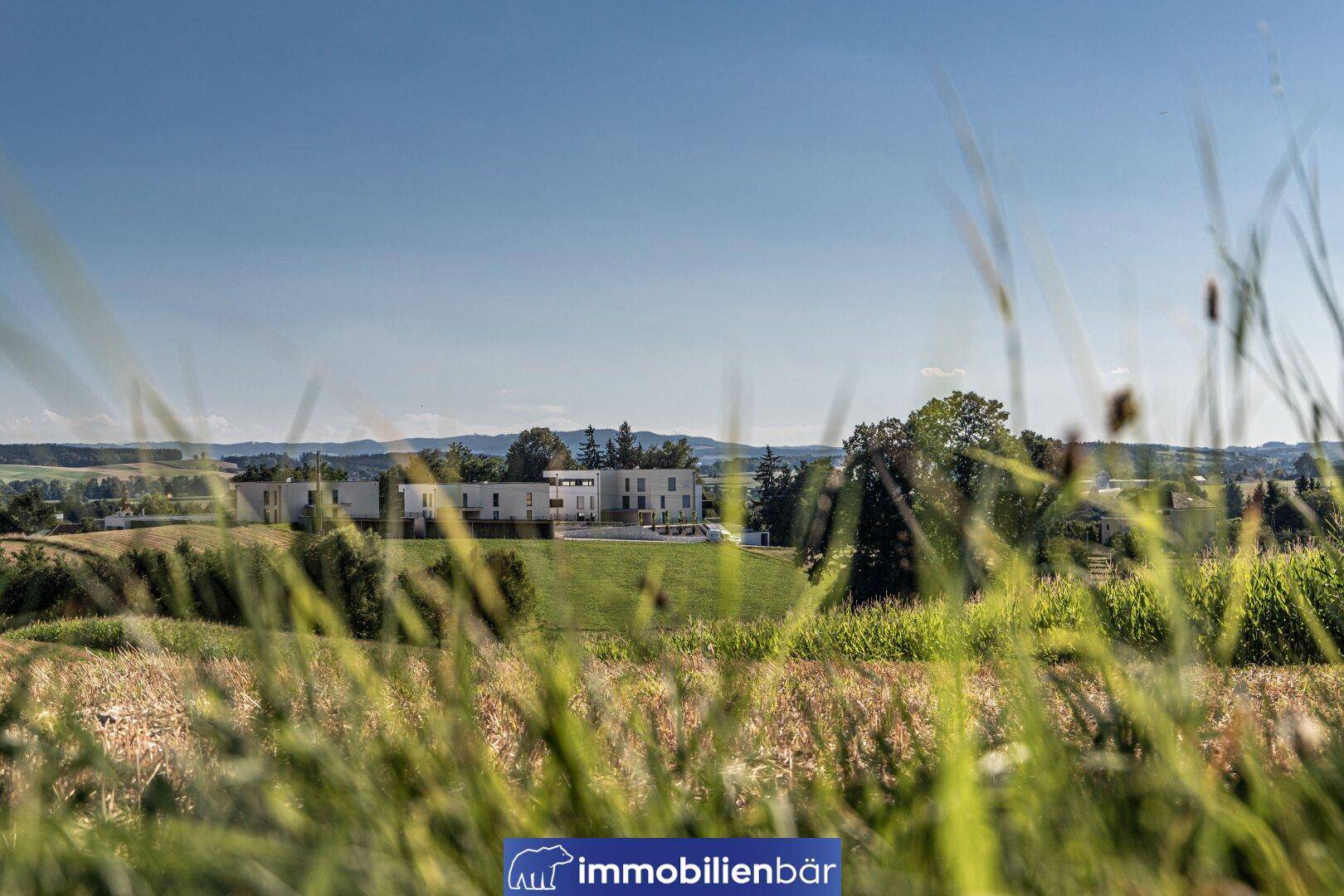 Weitläufiger Blick über grüne Felder auf moderne Wohngebäude in ländlicher Umgebung.