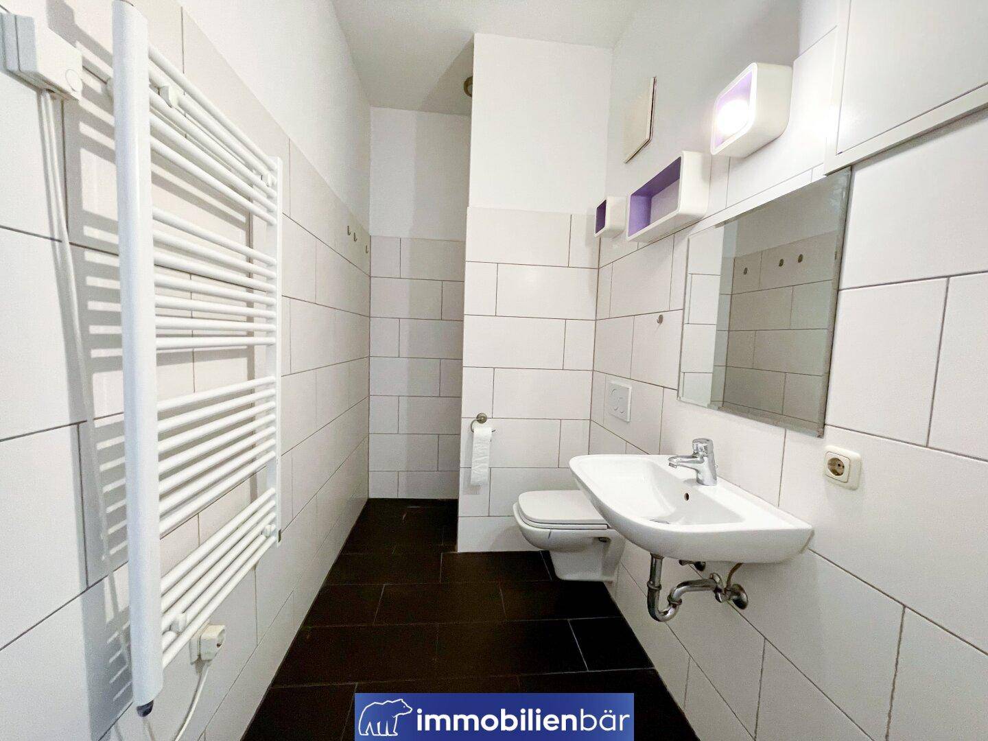 Funktionales Badezimmer mit Dusche, WC, Waschbecken und weiß gefliesten Wänden.
