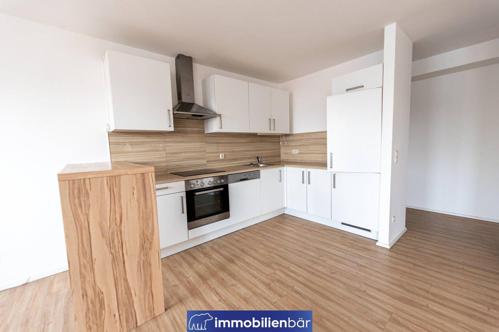 Helle Einbauküche mit weißen Fronten, Holzdetails und modernen Geräten in offenem Raum.