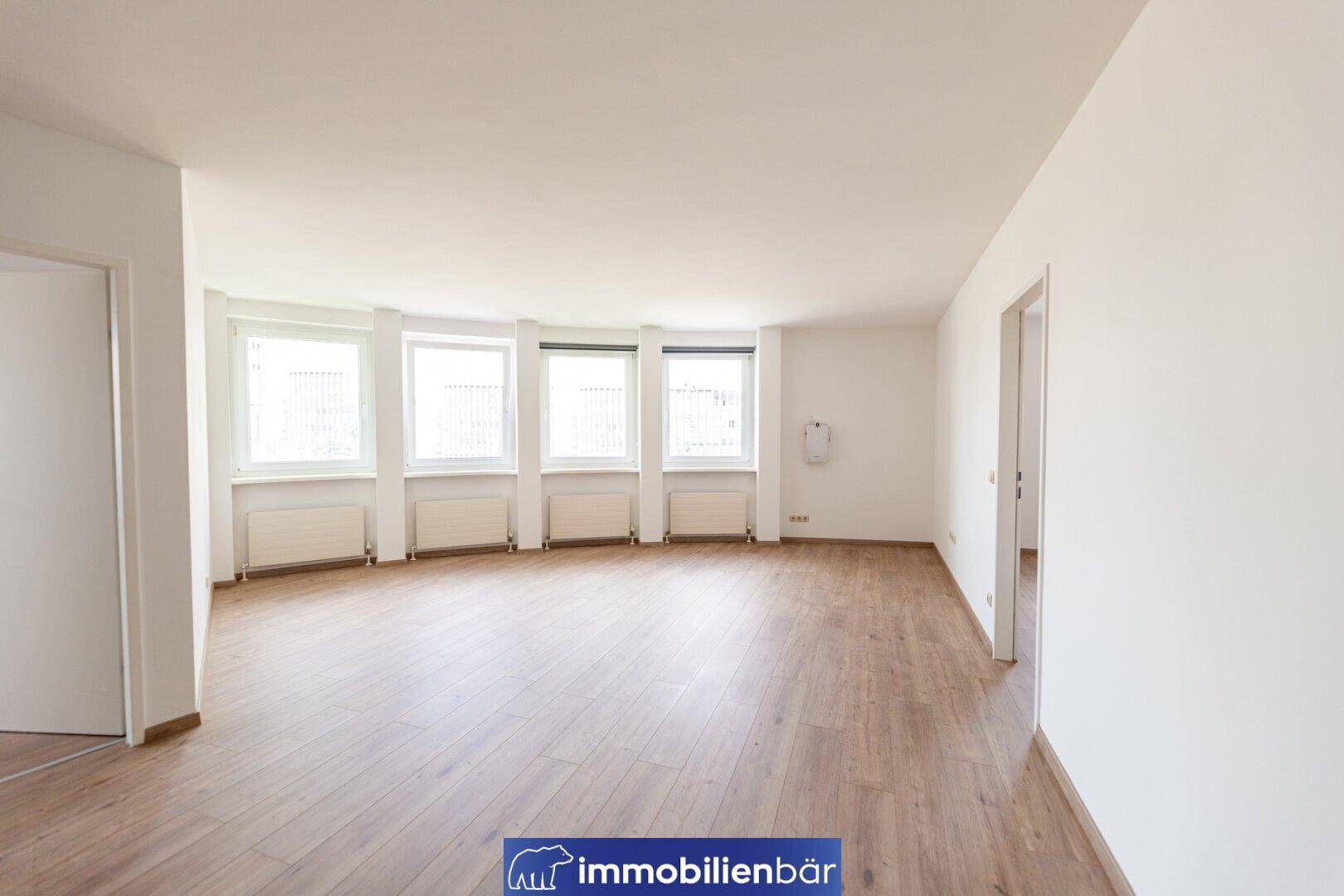 Geräumiges Wohnzimmer mit vielen Fenstern, Laminatboden und viel Tageslicht.