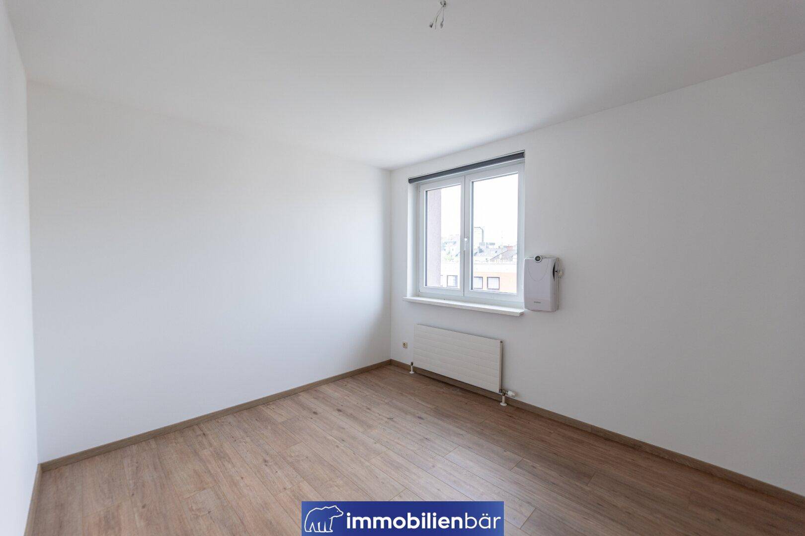 Leeres Schlafzimmer mit Laminatboden, weiß gestrichenen Wänden und einem Fenster.