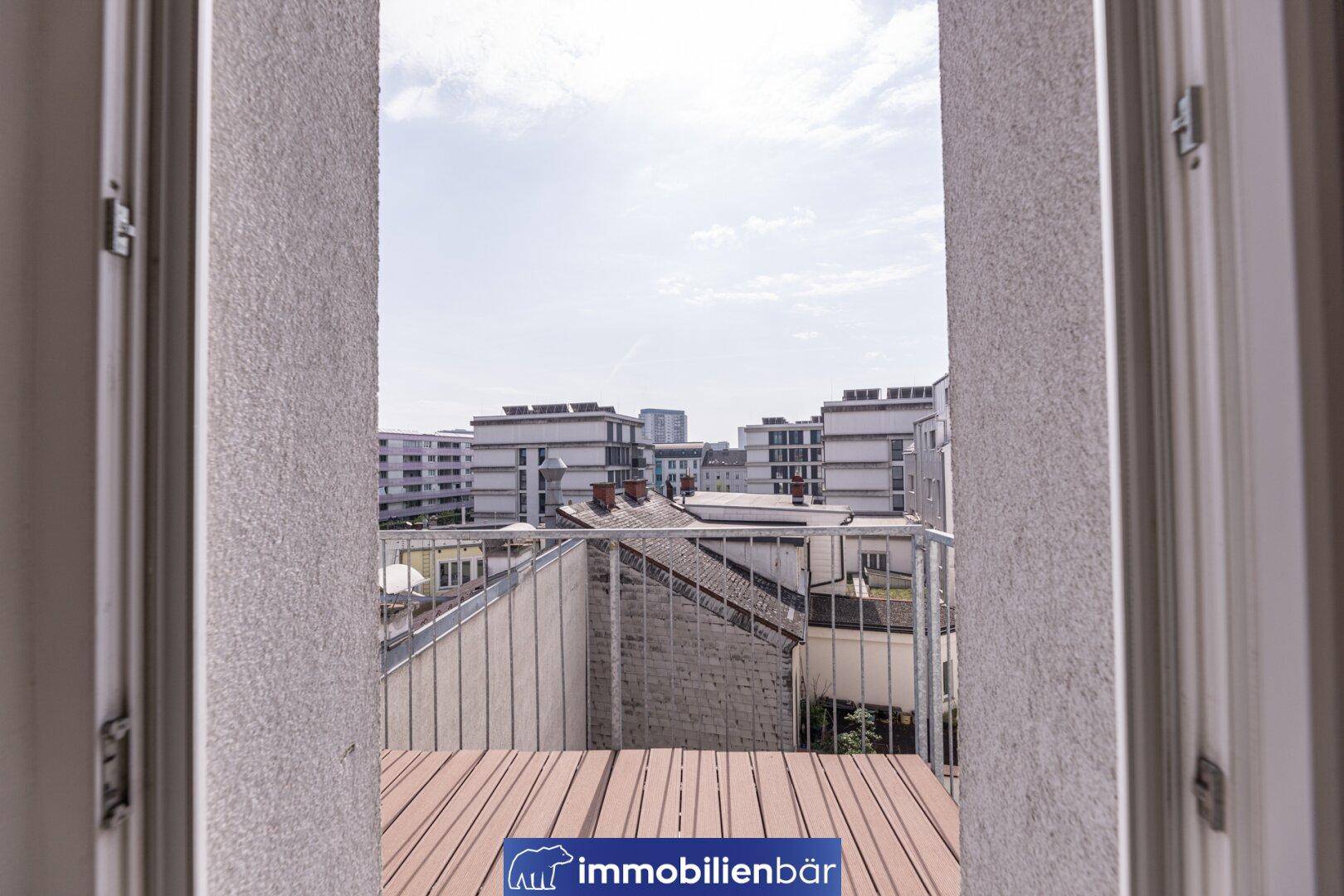 Kleiner Balkon mit Holzboden und Blick auf die umliegenden Gebäude der Stadt.