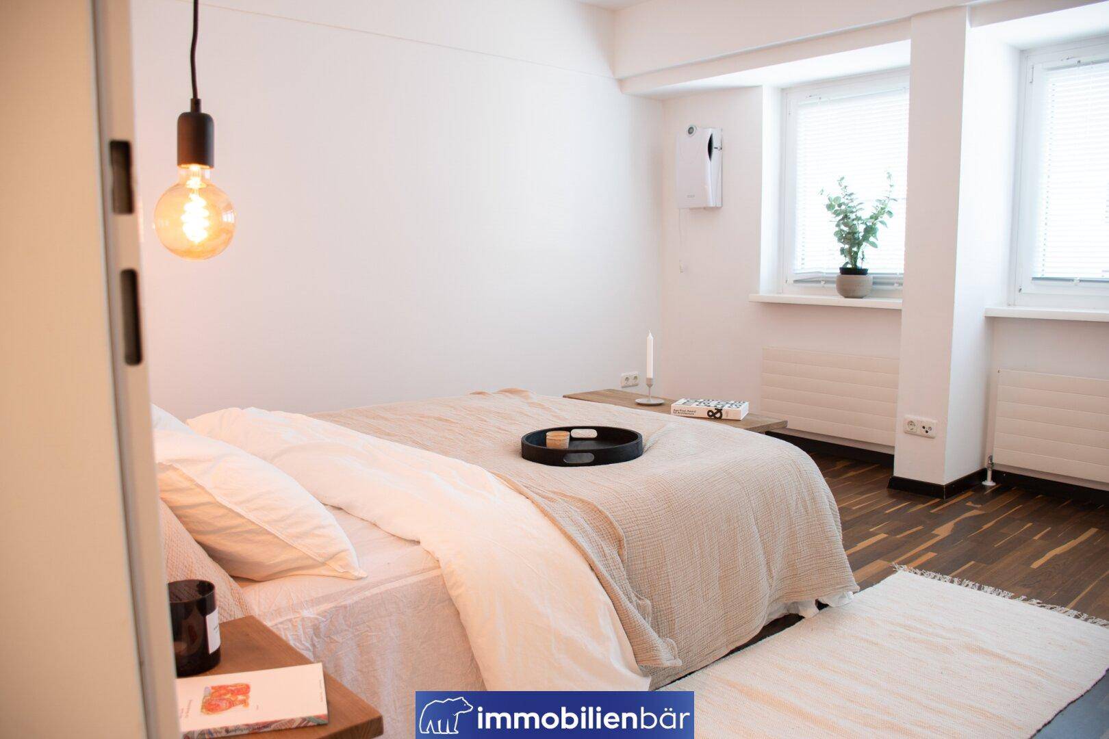 Gemütliches Schlafzimmer mit Doppelbett, Holzboden und zwei Fenstern.