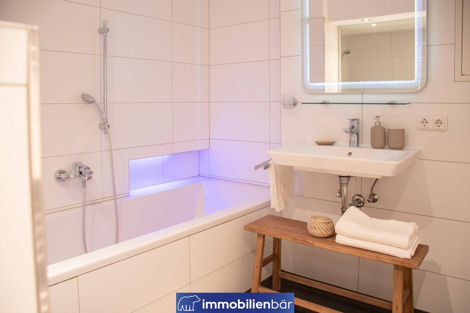 Modernes Badezimmer mit Badewanne, weiß gefliesten Wänden und beleuchteter Nische.