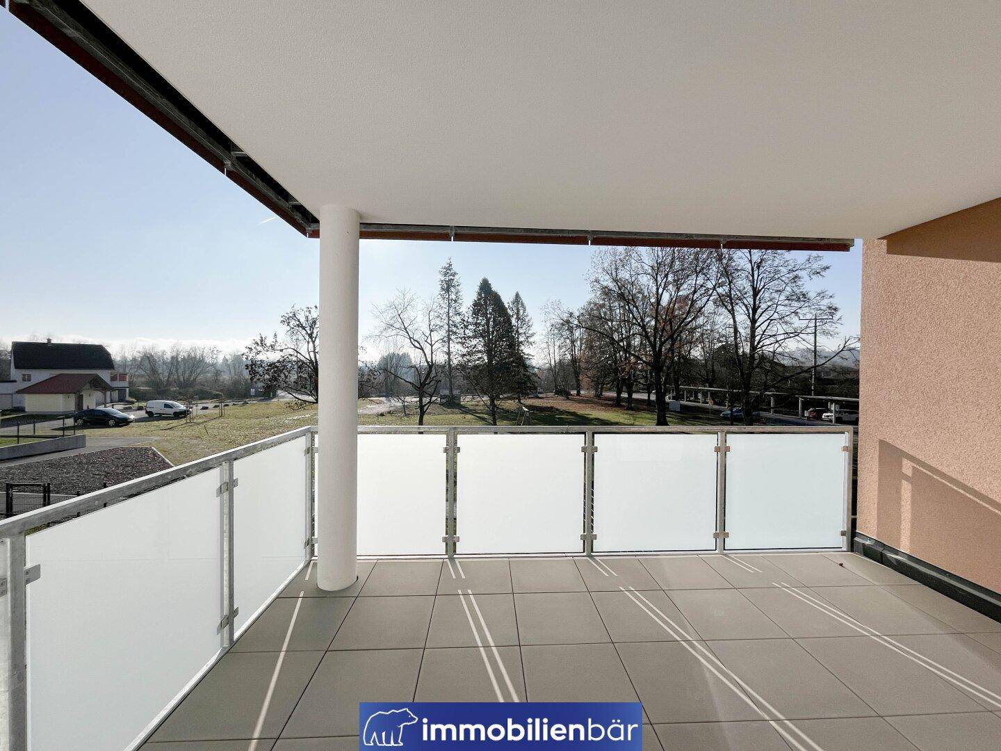 Geräumiger Balkon mit Fliesenboden und Milchglasgeländer, bietet einen weiten Blick ins Grüne.