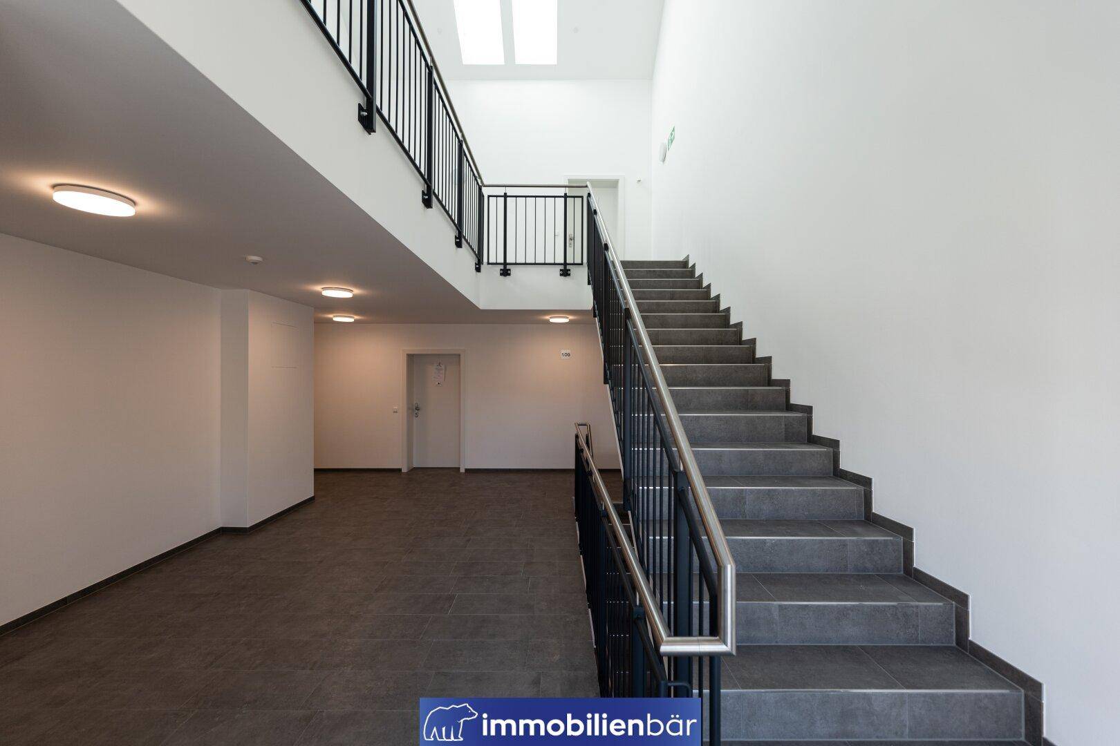 Helles Treppenhaus mit Fliesenboden und modernem Geländer, führt zu den oberen Etagen mit Oberlicht.