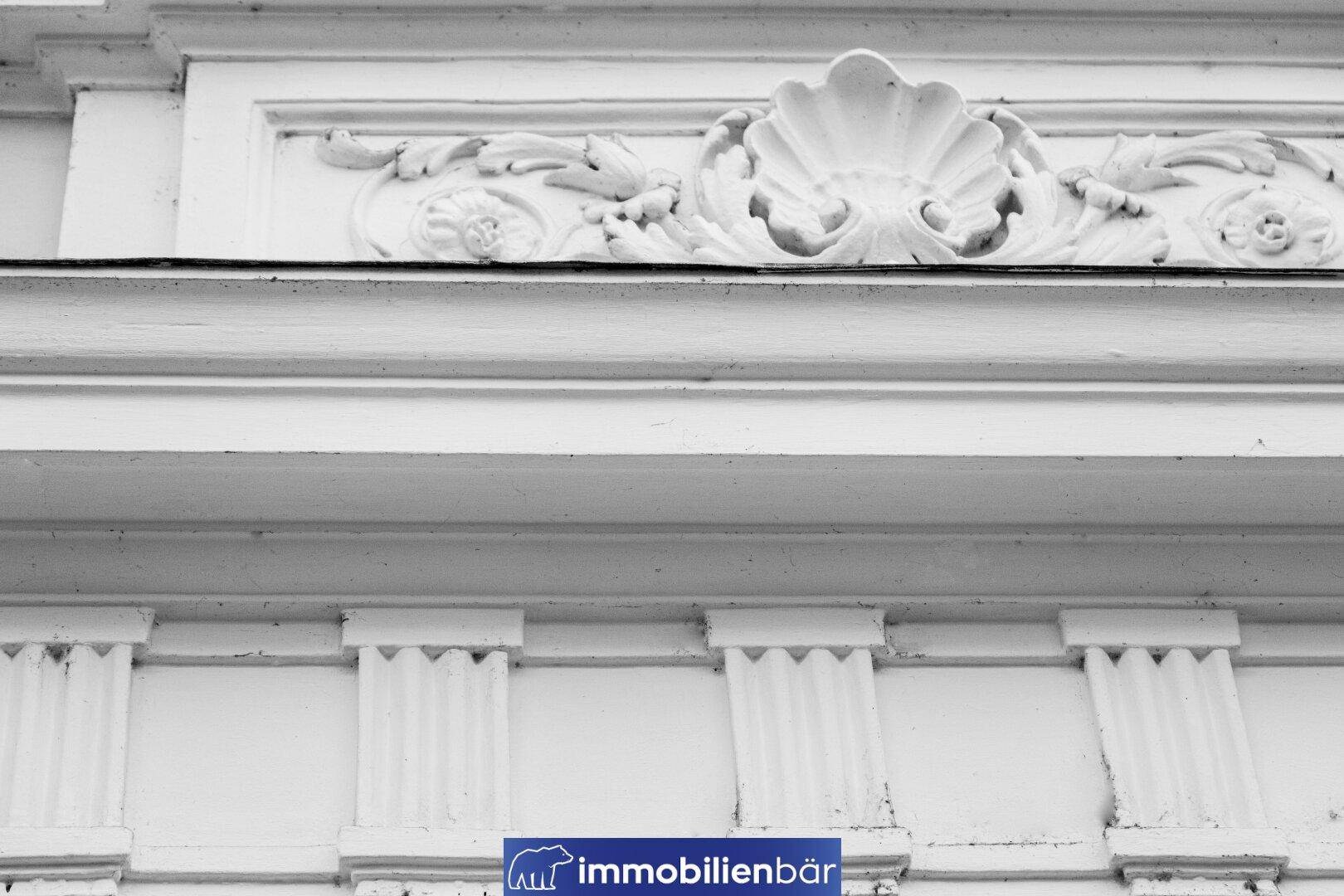 Nahaufnahme der weißen Stuckverzierungen an der historischen Fassade des Gebäudes.