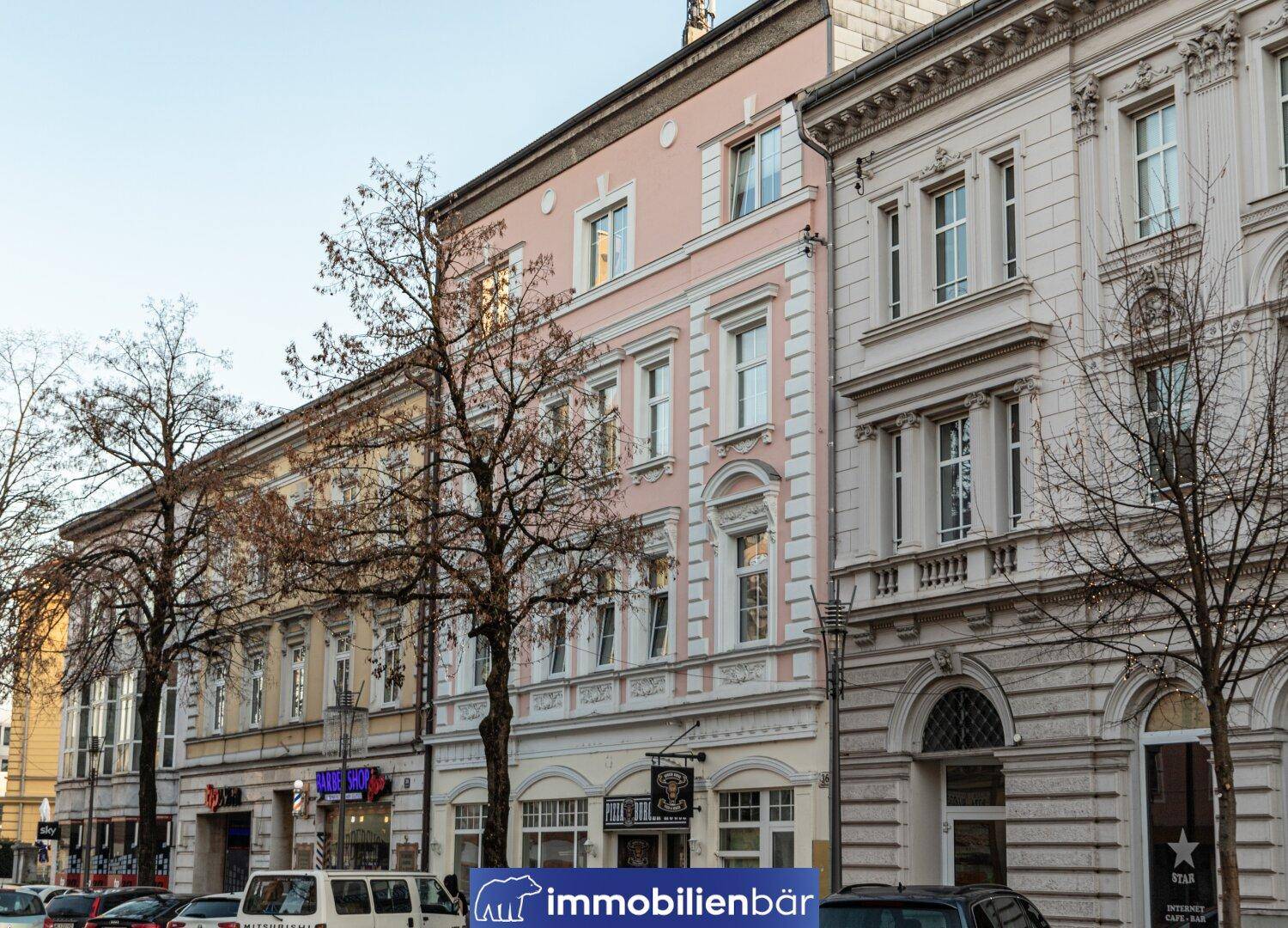 Historische Gebäudezeile mit rosa Fassade und Geschäften im Erdgeschoss an einer Straße.