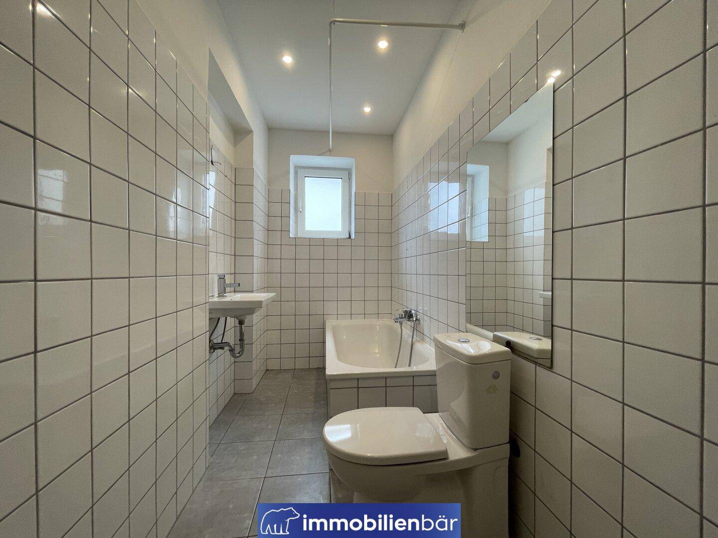 Gefliestes Badezimmer mit Badewanne, Toilette und kleinem Fenster für Tageslicht.