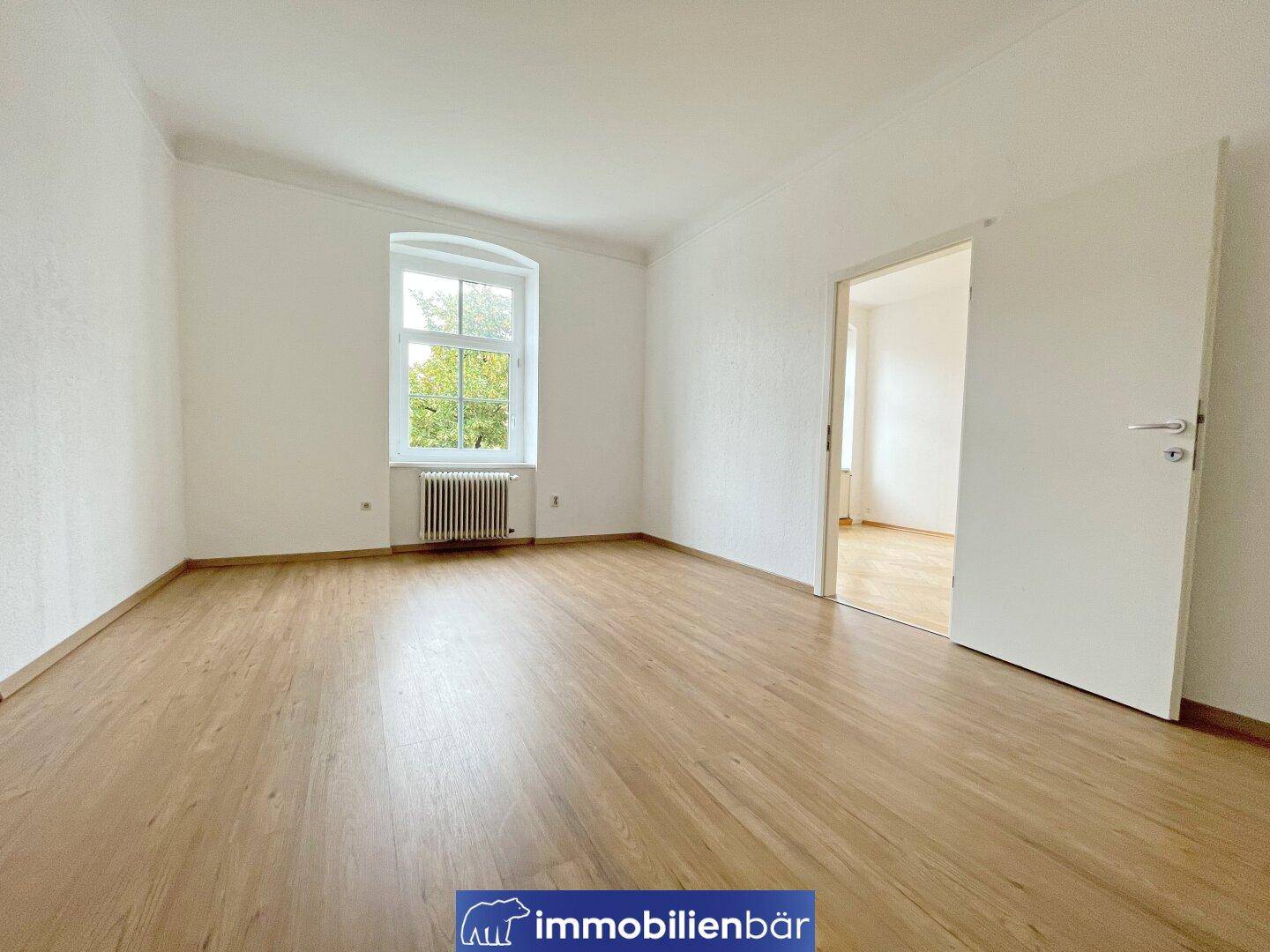 Geräumiges Schlafzimmer mit Laminatboden und einem großen Fenster mit Grünblick.
