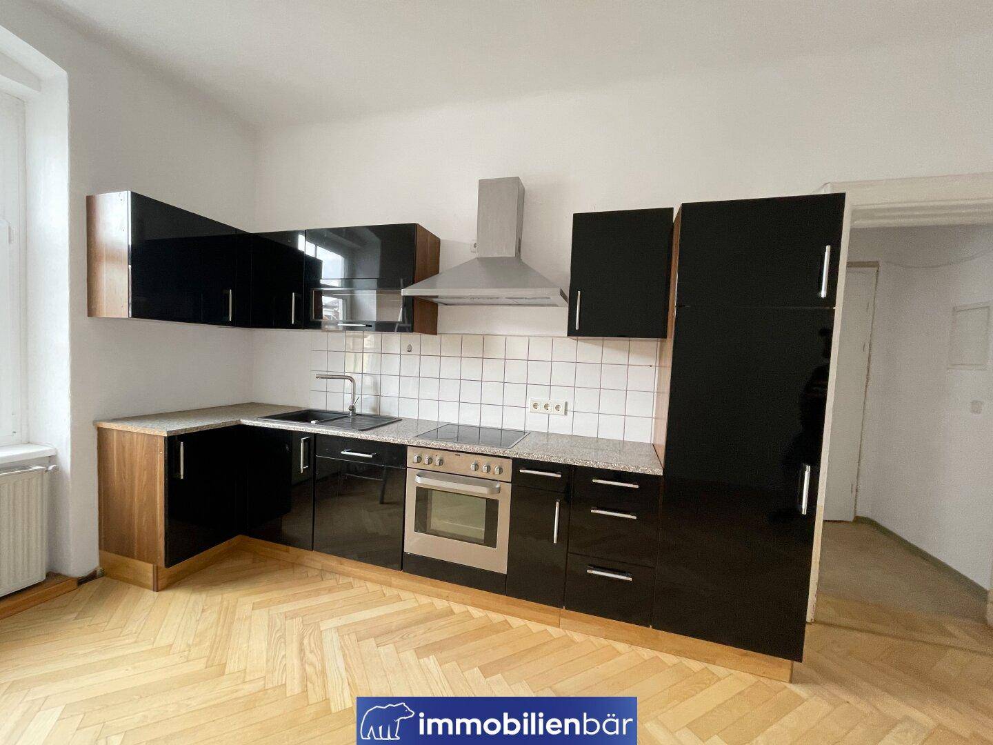 Moderne Einbauküche mit schwarzen Hochglanzfronten, Granitarbeitsplatte und Parkettboden.