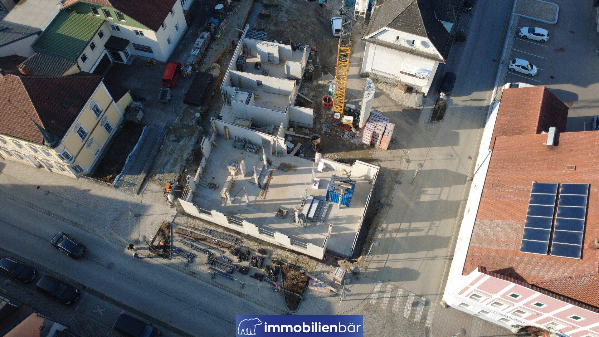 Luftaufnahme einer Baustelle mit Fundamenten und beginnendem Rohbau in städtischer Lage.