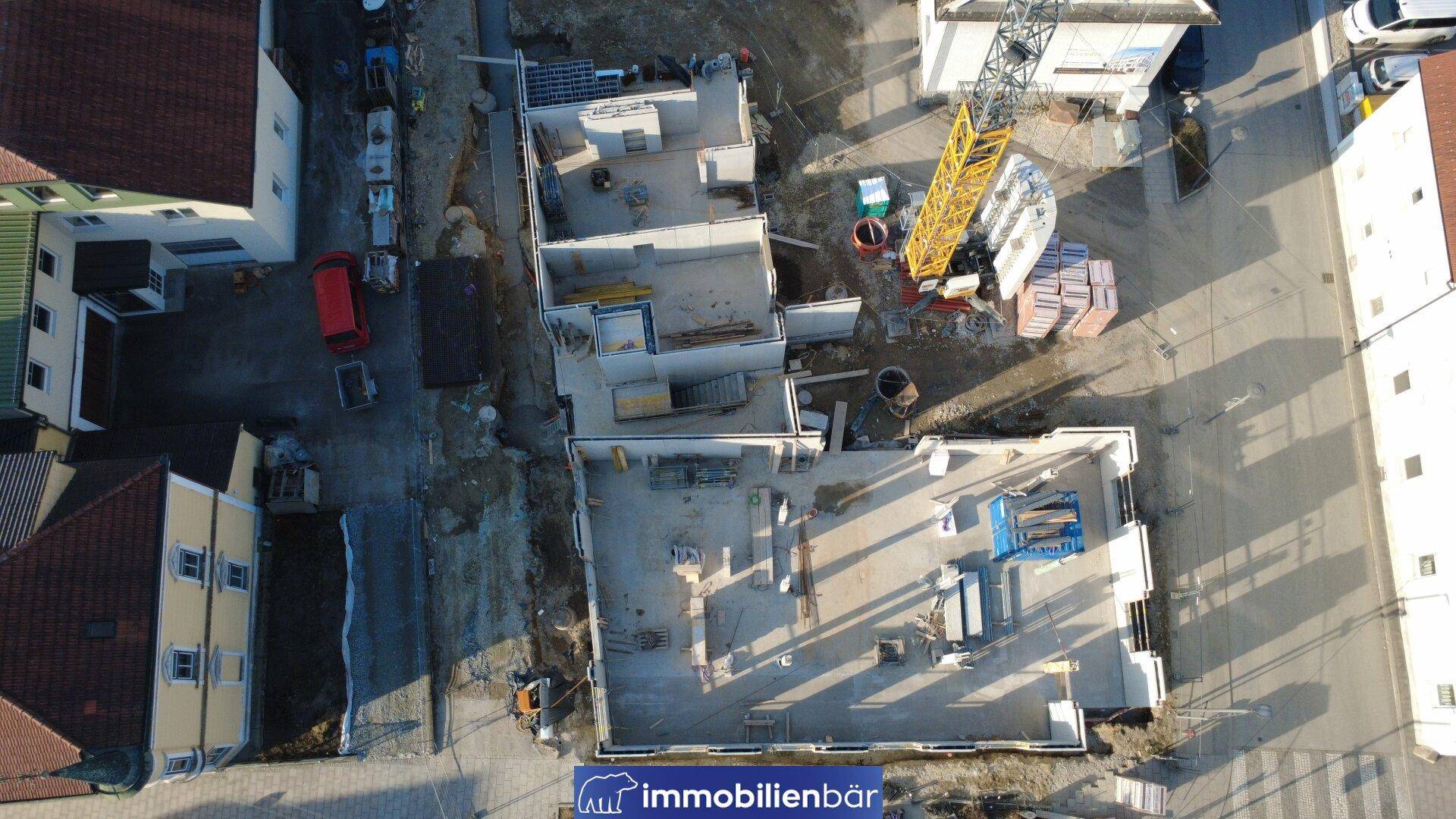 Draufsicht auf eine Baustelle mit mehreren Gebäudefundamenten und im Bau befindlichen Wänden.