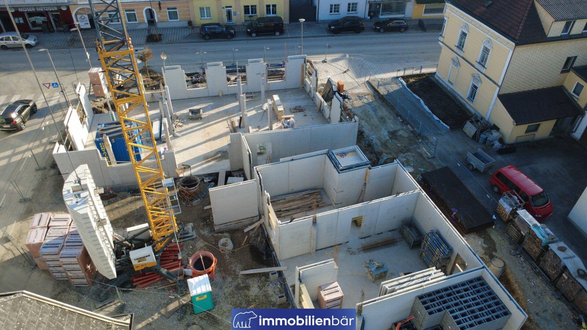 Nahaufnahme einer Baustelle aus der Vogelperspektive mit im Bau befindlichen Wänden und Kran.