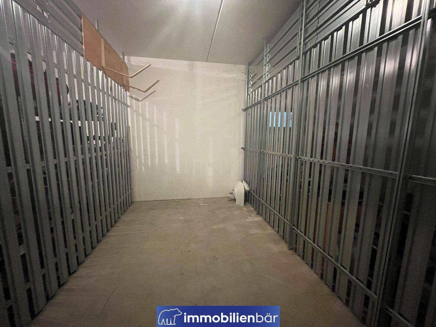 Geräumiger Abstellraum mit Metallabtrennungen und Betonboden, ideal für zusätzlichen Stauraum.