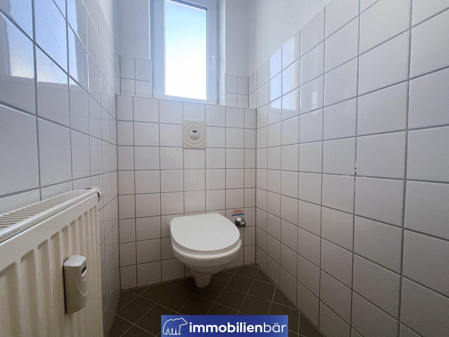 Gefliestes Gäste-WC mit wandhängender Toilette und kleinem Fenster für natürliche Belüftung.