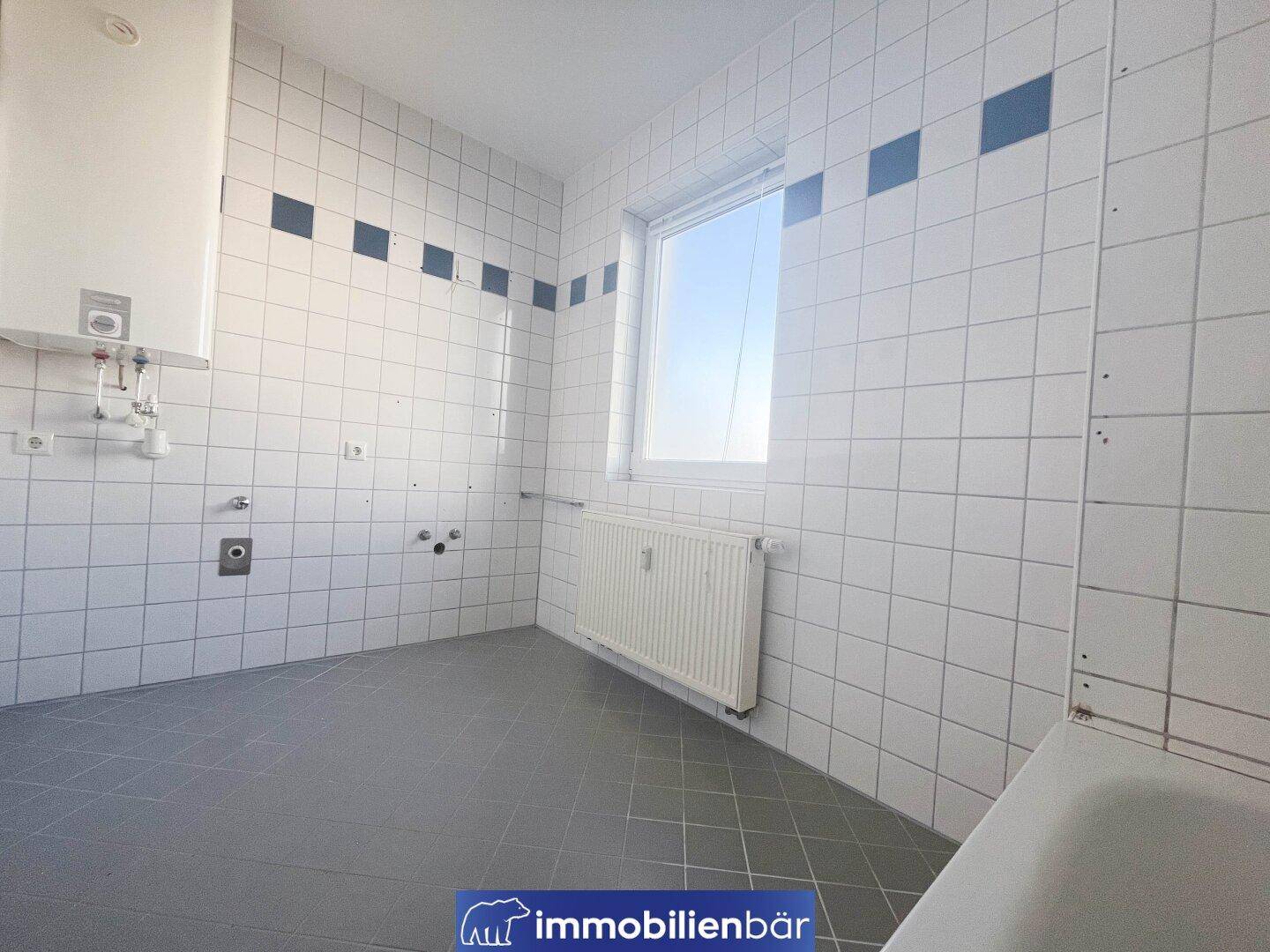 Geräumiges Badezimmer mit Fliesen, Fenster und Anschlüssen für Waschbecken und Waschmaschine.