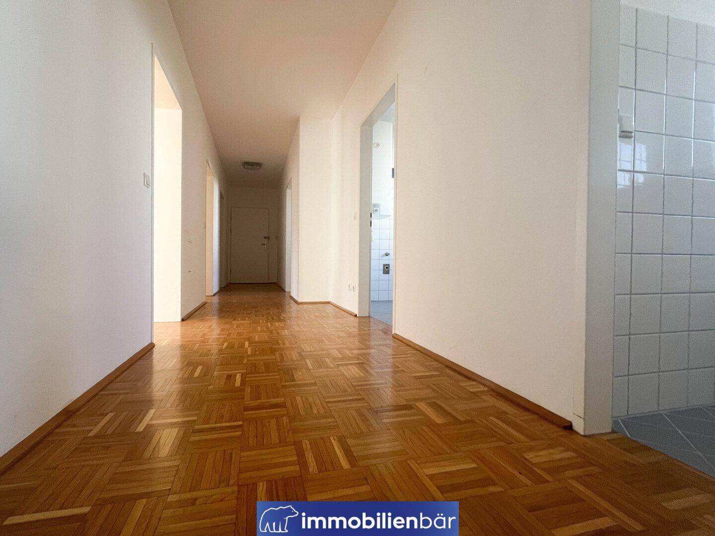 Langer, heller Flur mit Parkettboden und Zugang zu verschiedenen Räumen, inklusive Badezimmer.