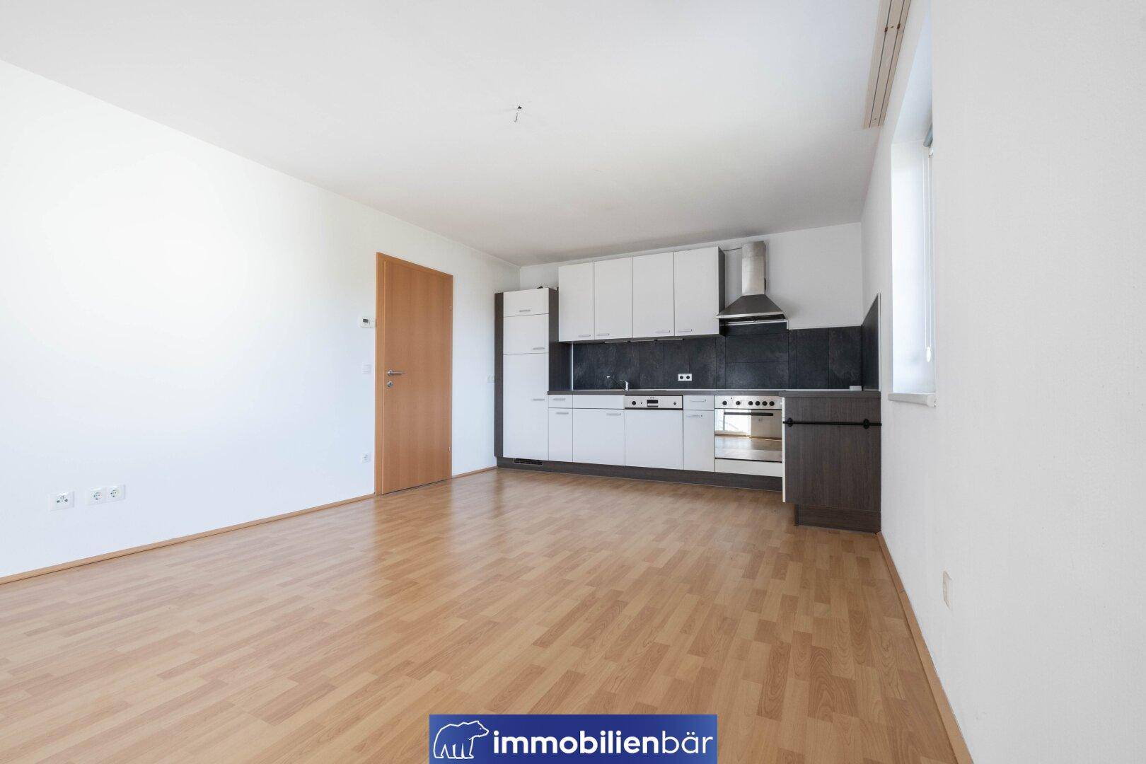 Funktionale Einbauküche mit weißen Oberschränken und dunkler Rückwand in einem geräumigen Zimmer.