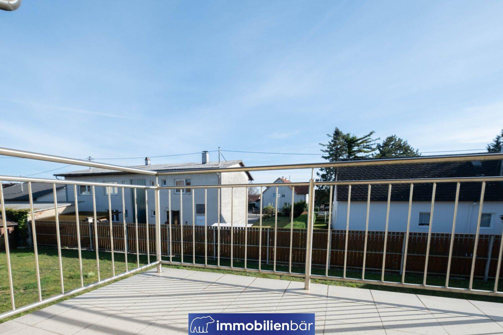 Heller Balkon mit Fliesenboden und Metallgeländer, bietet einen Blick auf die Nachbarschaft.