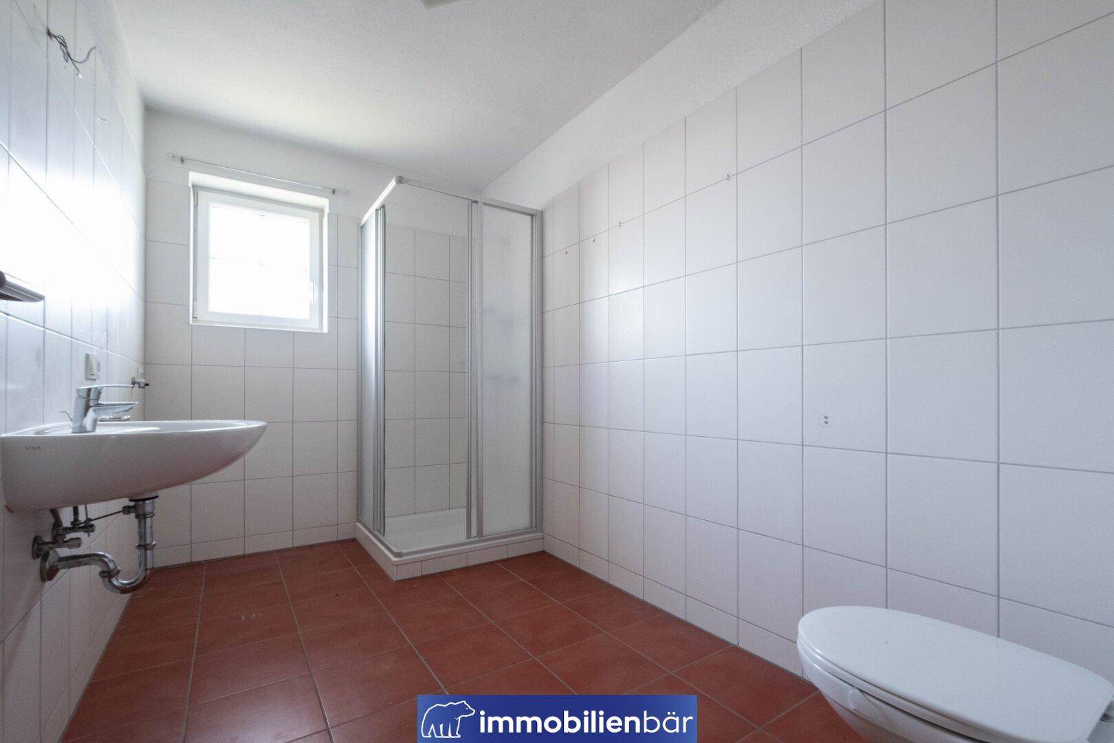 Funktionales Badezimmer mit Duschkabine, Waschbecken und WC, gefliest in Weiß und Terrakotta.