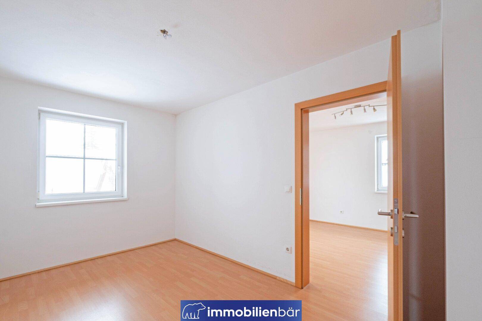 Leeres Zimmer mit Laminatboden und Holztürrahmen, das viel natürliches Licht erhält.
