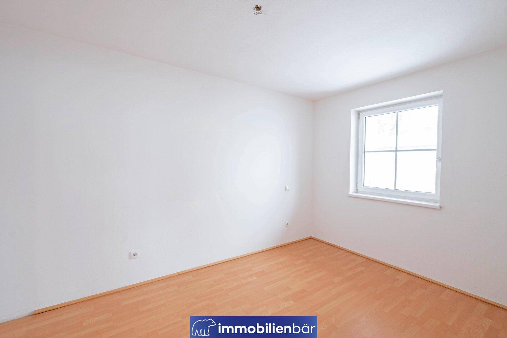 Ruhiges Schlafzimmer mit Laminatboden und einem Fenster, das für ausreichend Tageslicht sorgt.