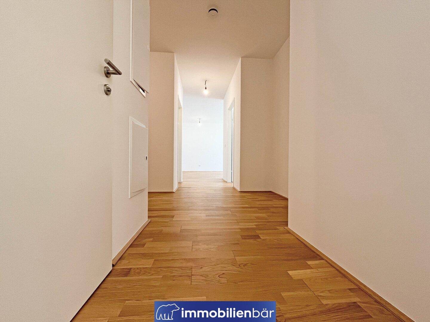 Langer, heller Flur mit Holzboden und weißen Wänden, der zu verschiedenen Zimmern führt.