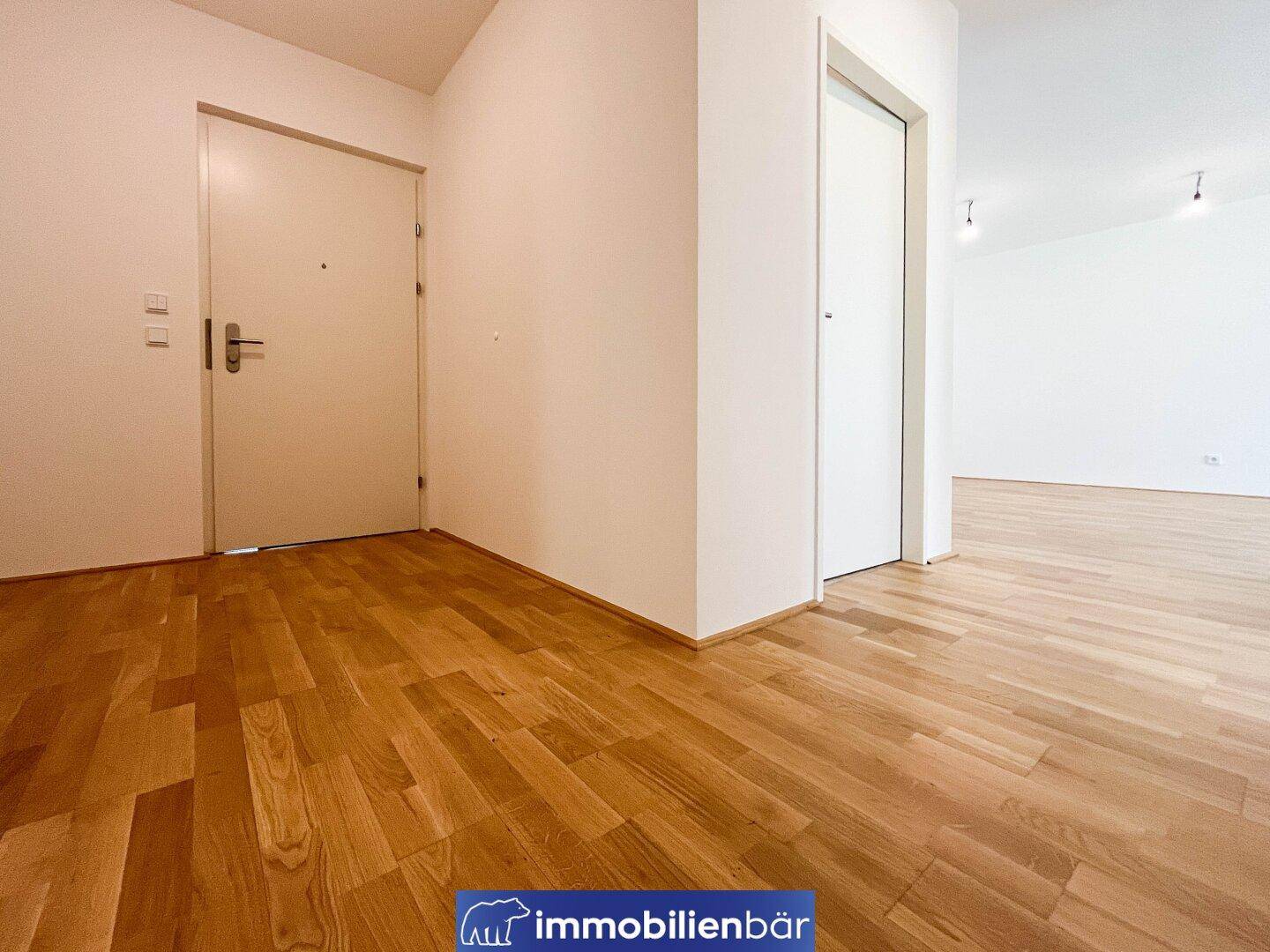Heller Eingangsbereich mit Holzboden und weißen Türen, der zu weiteren Räumen führt.