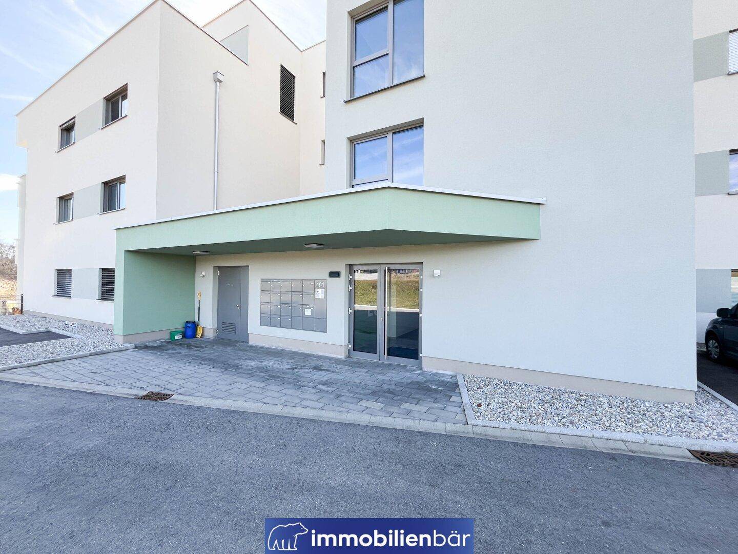Eingangsbereich eines modernen Mehrfamilienhauses mit Briefkästen und Zufahrt.