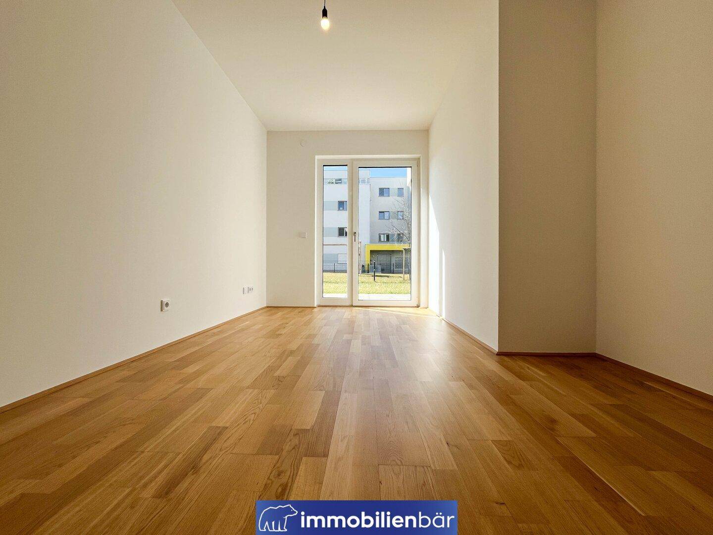 Helles, leeres Zimmer mit Holzboden und Zugang zum Garten, ideal für Wohnzwecke.