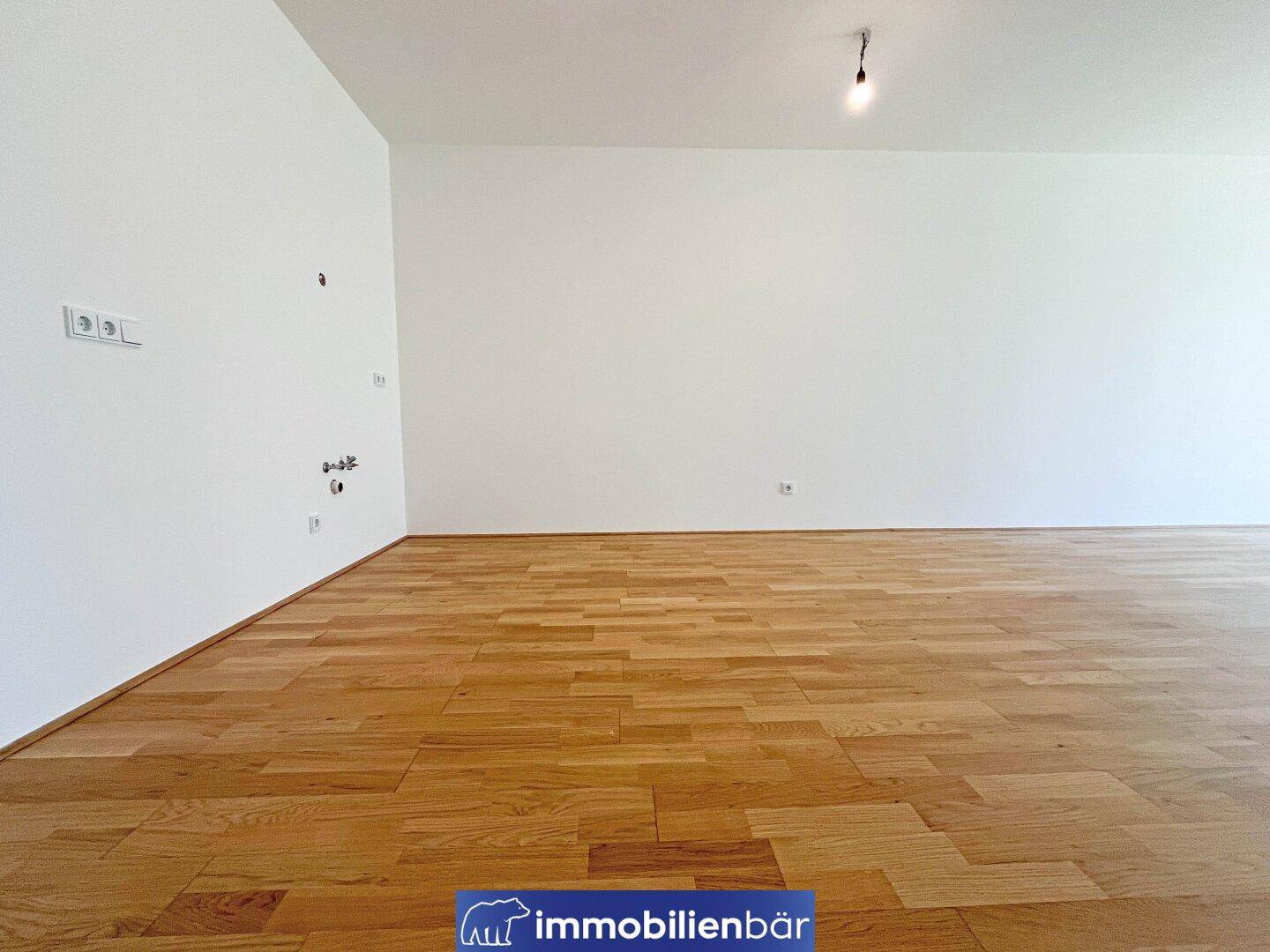 Leerer Raum mit Holzboden und Anschlüssen an der Wand, ideal für eine offene Küche oder Wohnbereich.