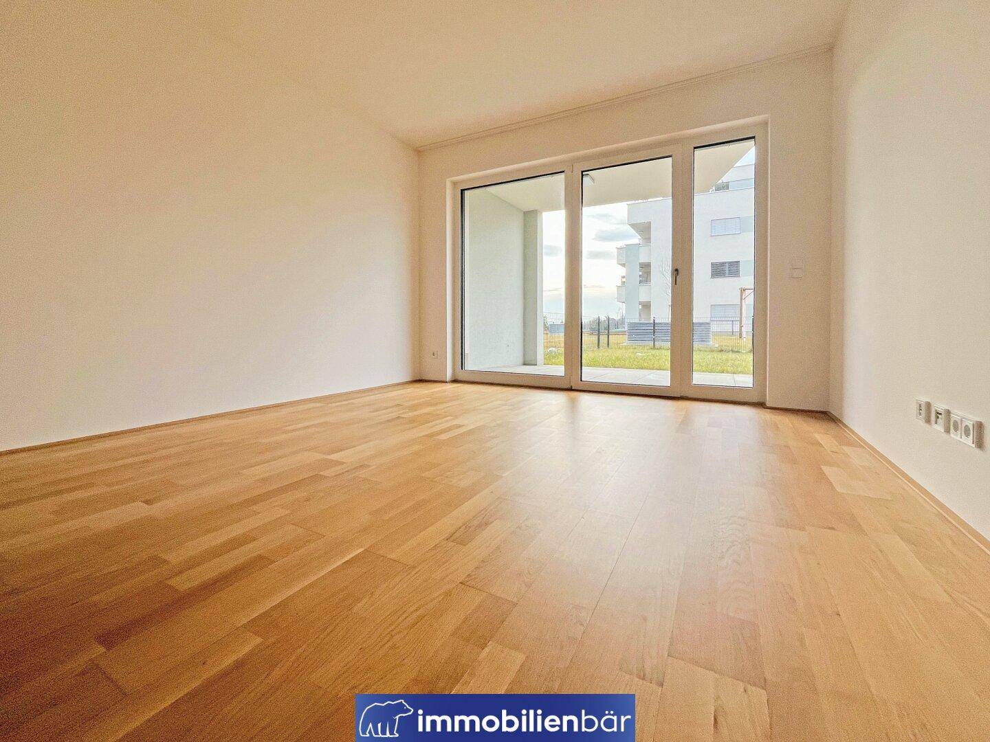 Helles Zimmer mit Holzboden und Zugang zu einem Außenbereich, bereit zur Einrichtung.