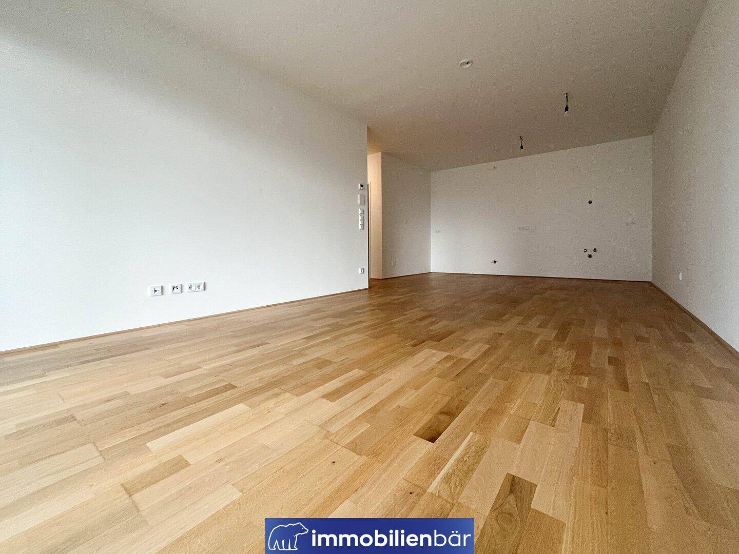 Geräumiges, leeres Zimmer mit hellem Holzboden und weißen Wänden, ideal für Wohnzwecke.