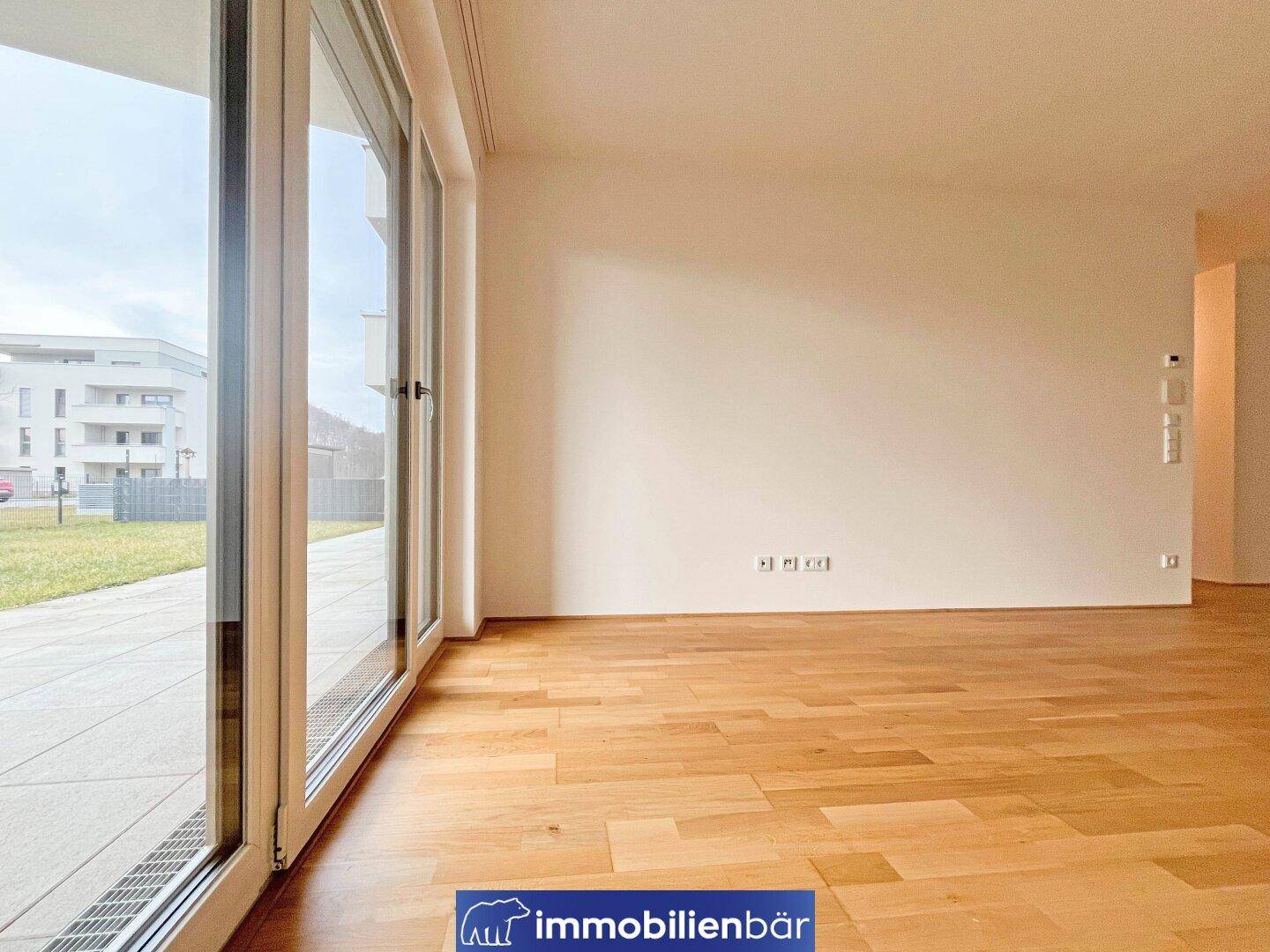 Helles, leeres Zimmer mit großen Fenstern und Holzboden, bereit zur individuellen Gestaltung.