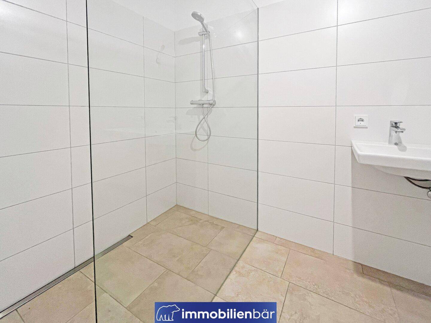 Modernes Badezimmer mit ebenerdiger Dusche, weißen Fliesen und Einzelwaschbecken.