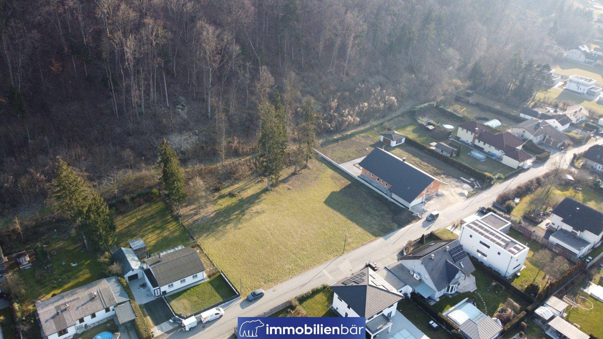 Weitläufige Luftaufnahme eines Wohngebiets mit unbebautem Grundstück und umgebender Natur.