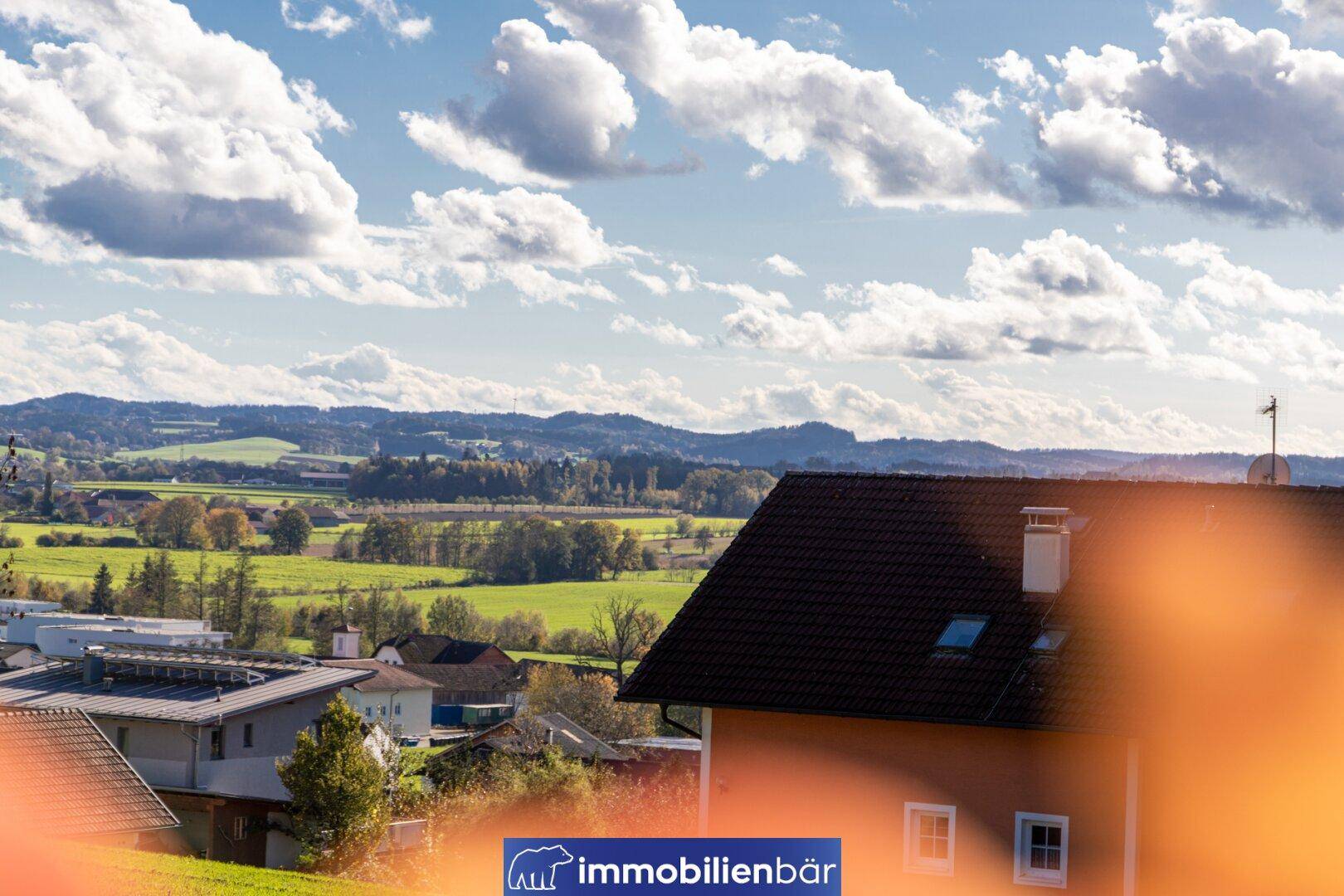 Weitläufige Landschaft mit grünen Feldern, Häusern und bewölktem Himmel an einem sonnigen Tag.