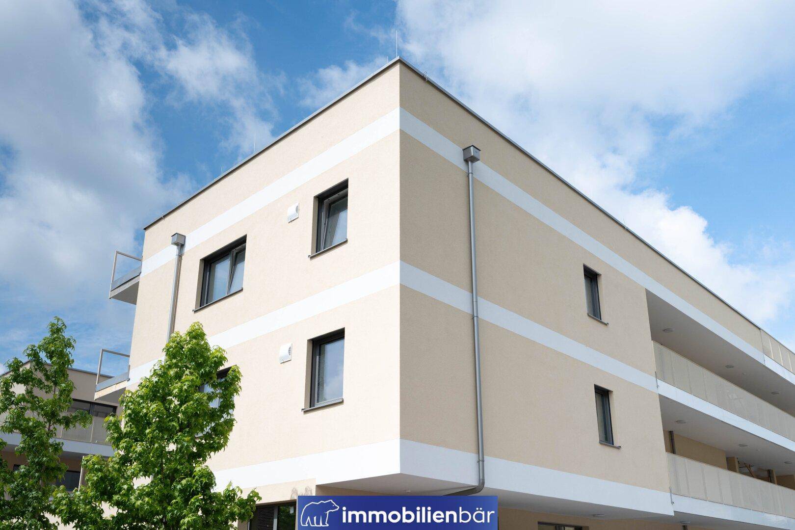 Außenansicht der modernen Gebäudeecke mit beiger Fassade und weißen Akzentstreifen unter blauem Himmel.