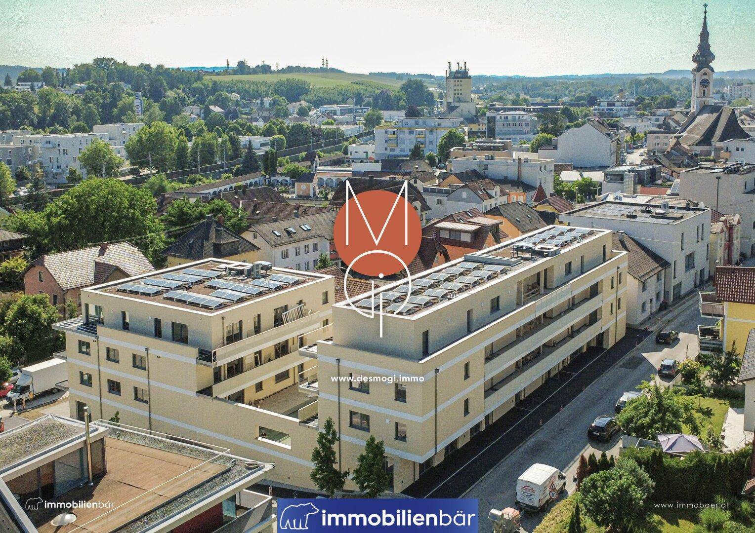 Luftaufnahme eines modernen Wohnkomplexes mit Solaranlagen auf den Dächern in städtischer Umgebung.