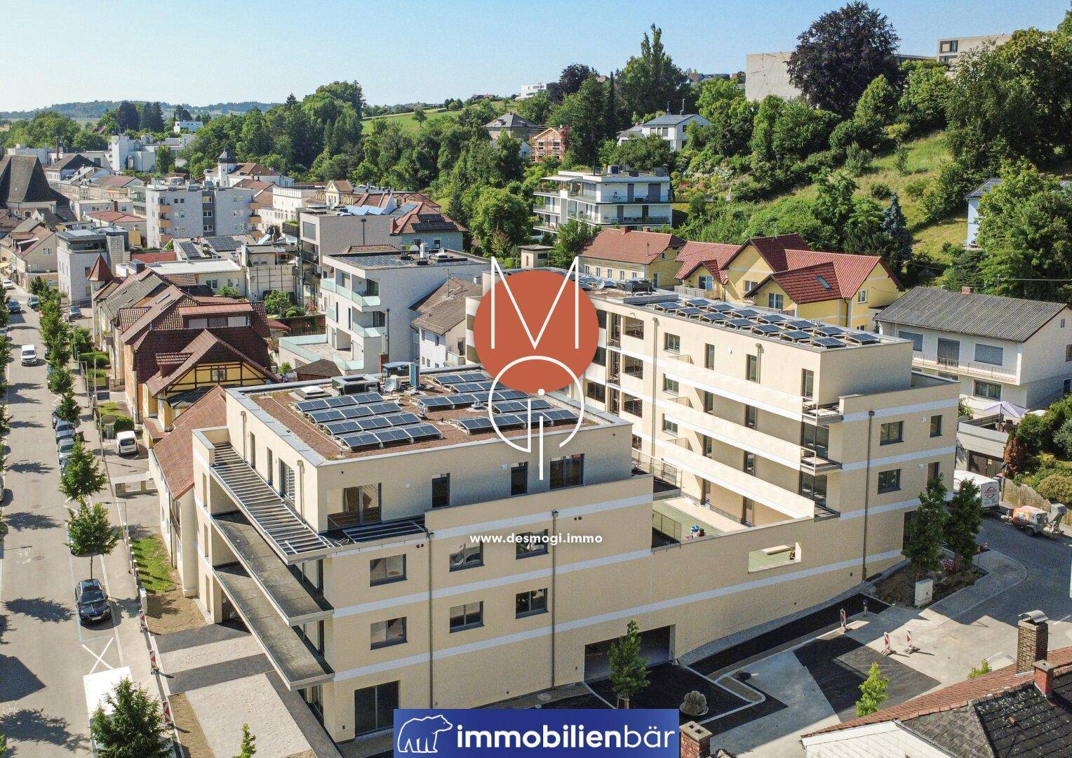 Panoramablick auf den modernen Wohnkomplex mit umliegender Bebauung und grünen Hügeln im Hintergrund.
