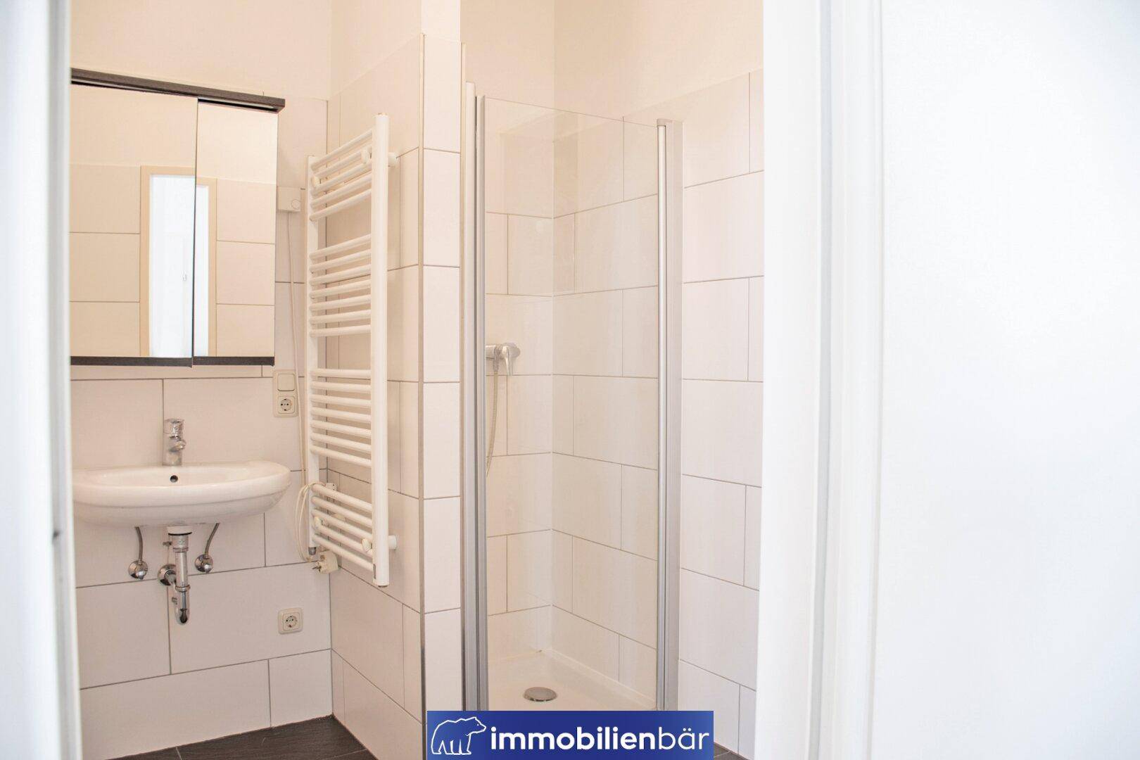 Modernes Badezimmer mit Dusche, Waschbecken und beheiztem Handtuchhalter, in hellen Fliesen.
