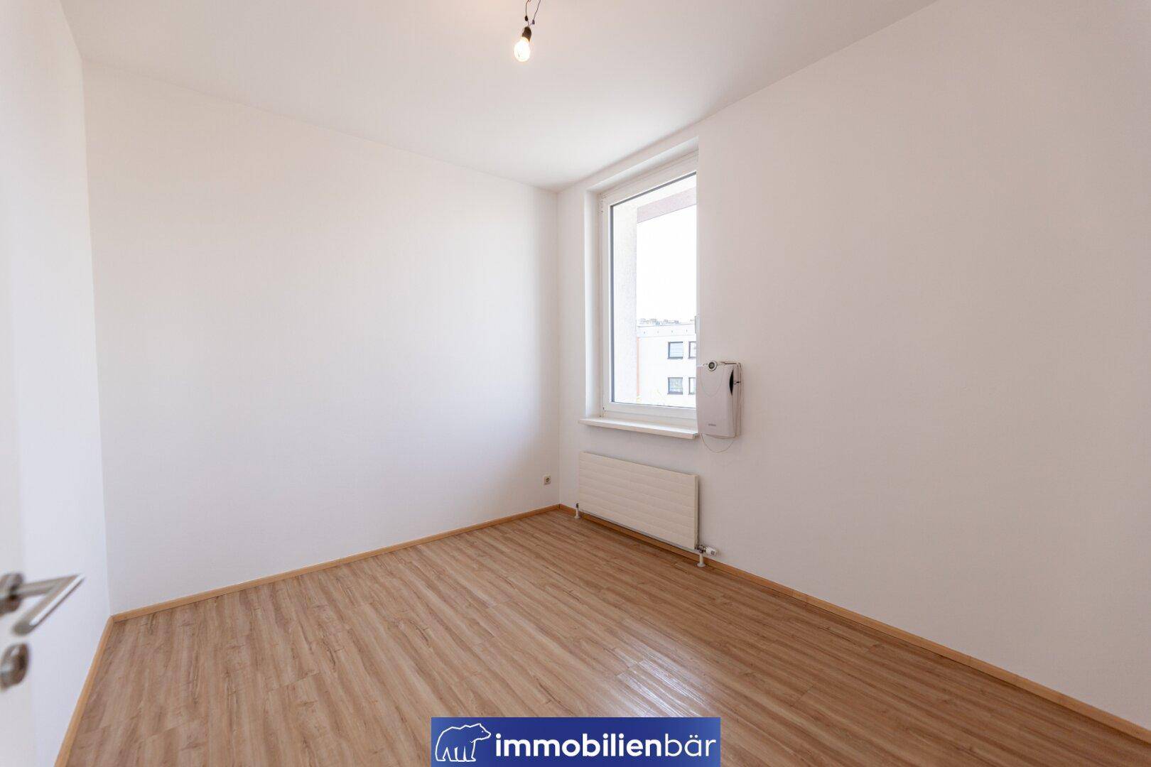Helles Zimmer mit Laminatboden und einem Fenster, das viel Tageslicht hereinlässt.