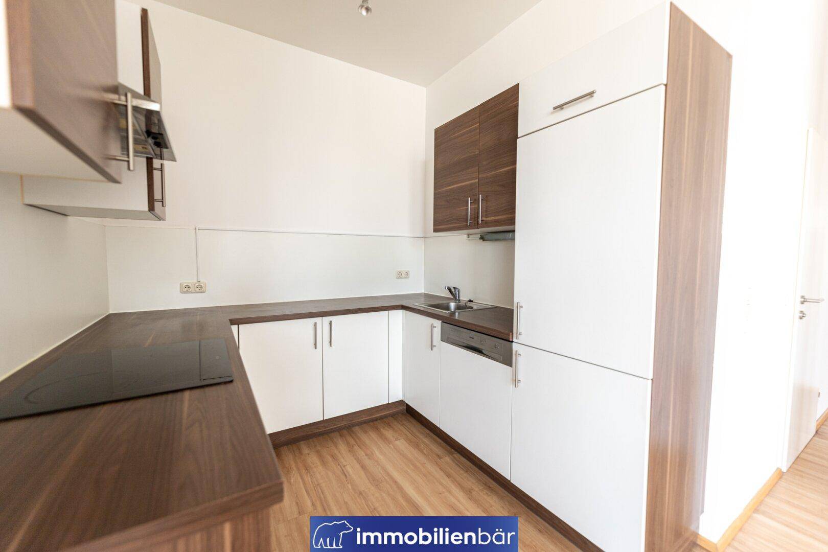 Moderne Küchenzeile mit weißen und holzfarbenen Schränken, ausgestattet mit Spüle und Kochfeld.