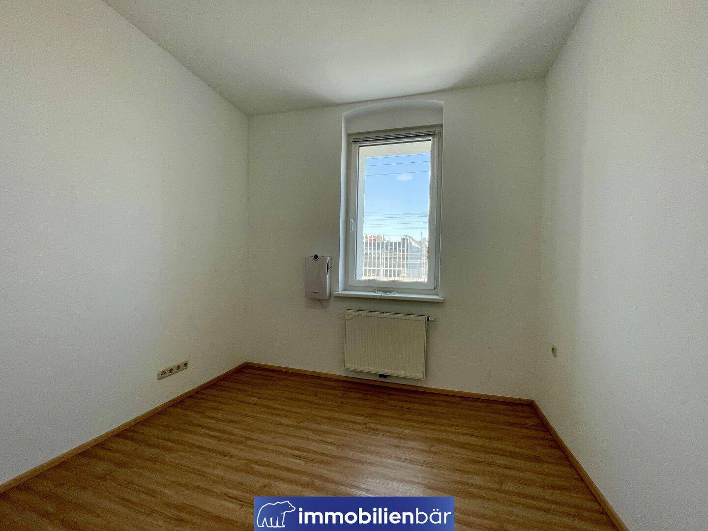 Ruhiges Schlafzimmer mit Laminatboden und einem Fenster, das viel Tageslicht hereinlässt.